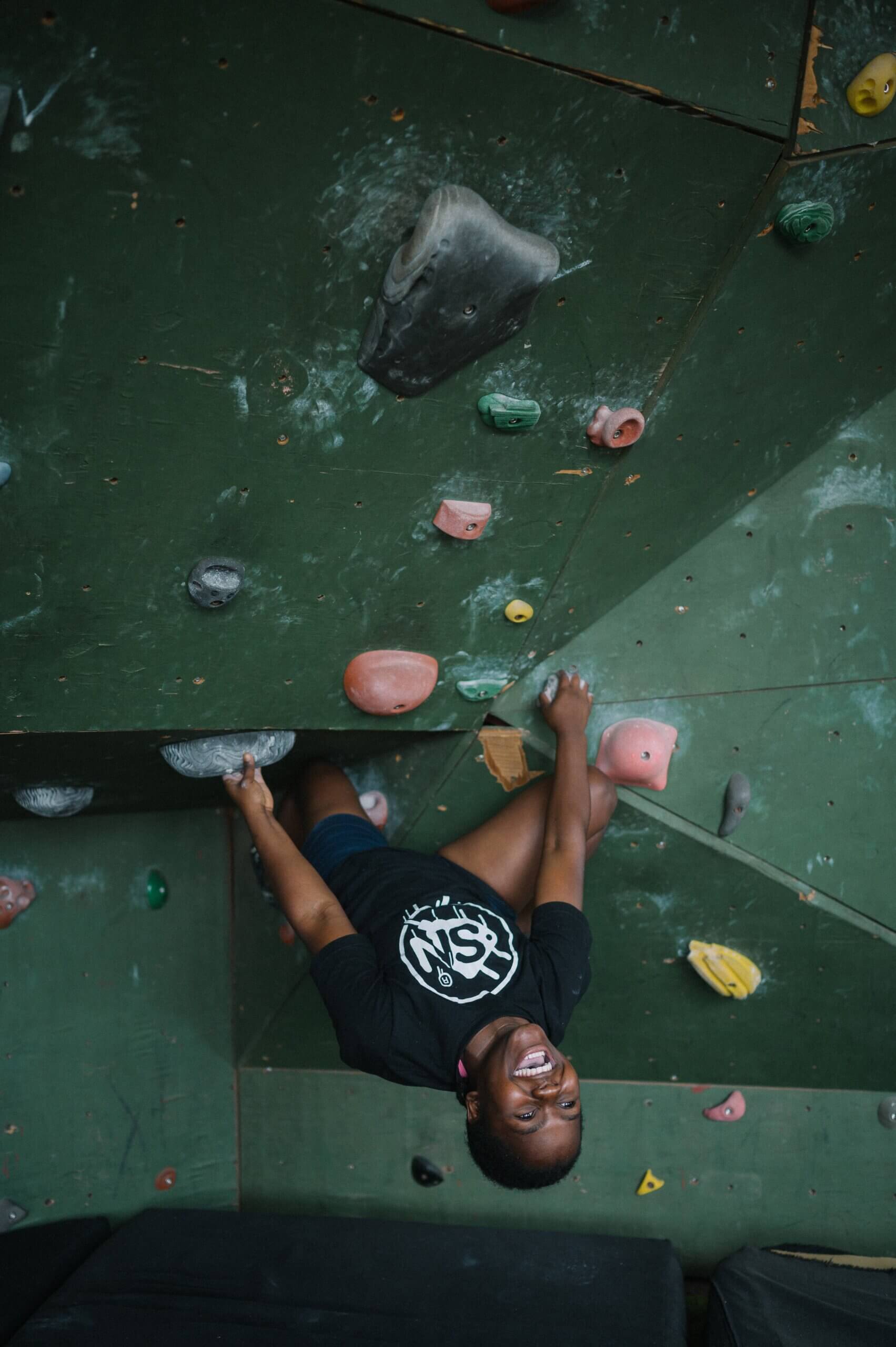 Shalom Maholo hanging upside down in the climbing gym.