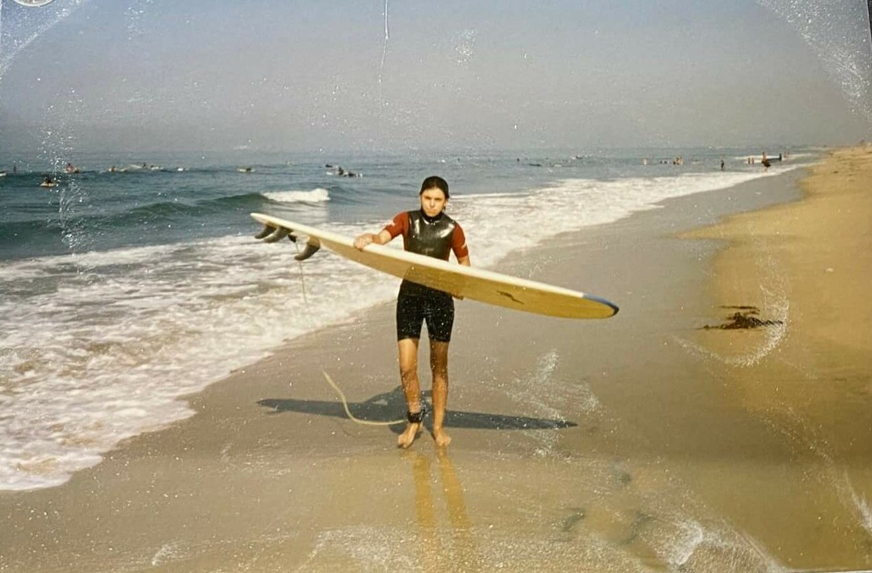 Ben Soto as a child with their surfboard on the beach.